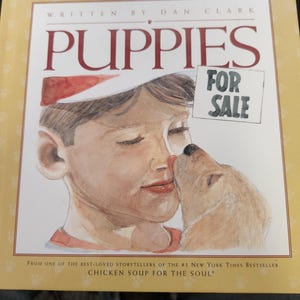 May include: Book cover with the title "PUPPIES" in red. The image shows a boy being kissed by a puppy, with the words "FOR SALE" and the author's name. The book is from the "Chicken Soup for the Soul" series.