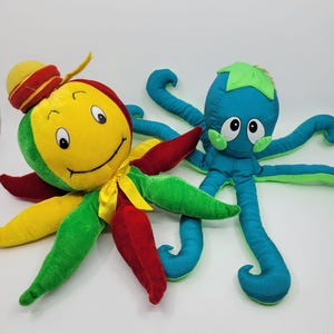 May include: Two plush octopus toys. The first is yellow, green, and red with a yellow ribbon and a small red hat. The second is blue with a green top accent. Both have large white eyes with black pupils and multiple long, curled tentacles.