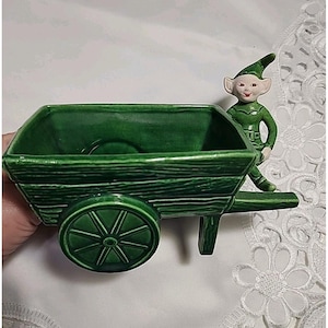 Maceta navideña vintage de cerámica verde con diseño de duende y carro de hadas.