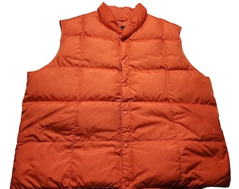 Op de afbeelding: Een feloranje gewatteerd vest met een vierkant stikpatroon, een hoge kraag en een sluiting aan de voorzijde met bijpassende oranje drukknopen. Het mouwloze kledingstuk heeft een gladde afwerking en een gewatteerde constructie.
