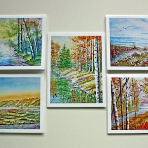 May include: Five framed watercolor paintings of landscapes. The paintings depict scenes of forests, rivers, and coastal views. The color palette includes greens, blues, yellows, and oranges, creating a natural and serene aesthetic.
