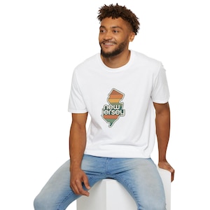 May include: A white short-sleeved t-shirt featuring a graphic of the state of New Jersey. The state outline is filled with horizontal stripes in shades of orange, yellow, and green, with the text "new jersey" written in white across the center.