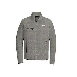 May include: A gray fleece jacket with a full-length zipper and two side pockets. The jacket has a high collar and the text "Your logo" is printed on the left chest. The North Face logo is on the right chest.
