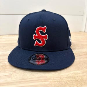 Puede incluir: Gorra de béisbol azul marino con una letra "S" roja y blanca bordada en la parte delantera. La gorra tiene una visera plana y una pegatina "9FIFTY SNAPBACK". Fabricada con material duradero.