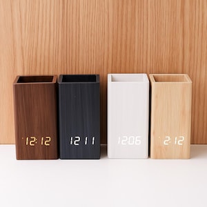 Peut inclure: Quatre organiseurs de bureau rectangulaires en bois, de tons marron, noir, blanc et bois clair. Chaque organisateur affiche une horloge numérique avec l'heure. Les organisateurs sont disposés en rangée sur un fond en bois clair.