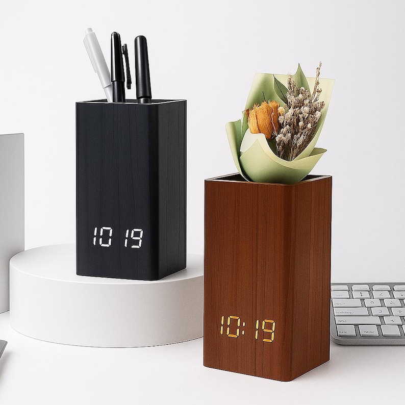 May include: Two wooden desk tidies. One is black and holds pens, the other is brown and holds a small bouquet. Both have a digital clock display showing 10:19.