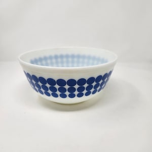 May include: A white milk glass bowl featuring a repeating pattern of solid dark blue circles arranged in three horizontal rows around the exterior. The interior of the bowl is plain white, with the blue circle pattern visible through the translucent glass.