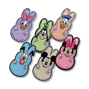 May include: Six embroidered patches featuring Disney characters in Easter bunny costumes. Daisy Duck in purple, Goofy in green, Donald Duck in peach, Minnie Mouse in pink, Pluto in blue, and Mickey Mouse in beige. Each patch has a black border.