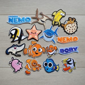 May include: A collection of embroidered patches featuring characters and text from the animated film "Finding Nemo." The patches include Nemo, Dory, a shark, and other sea creatures in vibrant colors. The patches are designed for clothing or accessories.
