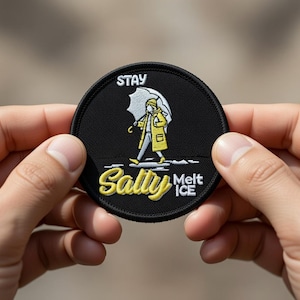 Puede incluir: Un parche redondo negro con las palabras "STAY Salty Melt ICE" en letras blancas y amarillas. El parche presenta una ilustración de una persona con un impermeable amarillo y un paraguas. El parche está sostenido entre dos manos.