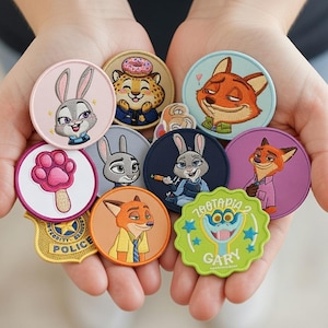 Può includere: Una collezione di toppe ricamate con personaggi del film d'animazione "Zootropolis". Le toppe sono rotonde, con vari disegni tra cui Judy Hopps, Nick Wilde e altri personaggi. I colori includono rosa, blu, arancione e verde.