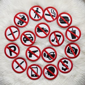 May include: A selection of circular patches with red borders and white centres, each displaying a black symbol crossed out with a red line. Symbols include a bomb, a person walking, a cigarette, a hamburger, a knife, a car, a truck, a musical note, a drink, a parking sign, a gun, a car crash, a camera, a phone, a person talking, and a dollar sign.