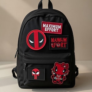 Peut inclure: Sac à dos noir orné de patchs rouges et blancs. Les patchs incluent le logo Deadpool, les mots "MAXIMUM EFFORT" et un Hello Kitty sur le thème de Deadpool. Le sac à dos a une poche avant et une poignée supérieure.