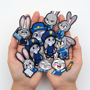 May include: A collection of embroidered patches featuring the character Judy Hopps from the animated film Zootopia. The patches depict Judy in various poses, wearing her police uniform and holding a carrot. The patches are in shades of blue, gray, and pink.