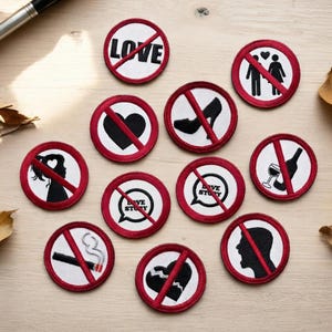 Può includere: Una collezione di toppe rotonde ricamate con bordi rossi e centri bianchi. Ogni toppa presenta una grafica nera con una barra rossa, tra cui un cuore, un tacco alto e la parola "LOVE".