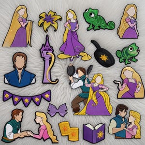 May include: A collection of embroidered patches featuring characters and elements from a fairy tale. The patches include a princess in a purple dress, a chameleon, a tower, and other related designs. The patches are in various colors.