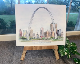 May include: Watercolor illustration of the Gateway Arch in St. Louis, Missouri, with a cityscape in the background. The artwork is displayed on a small wooden easel. The text "Gateway Arch, St. Louis, Missouri" is printed below the image.