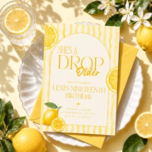 May include: A yellow birthday invitation with the text "She's a Drop Older" and "Lexi's Nineteenth Birthday". The invitation features watercolor lemon slices and a matching yellow envelope. A glass of water with a lemon slice is also visible.