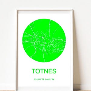 May include: A framed print featuring a neon green circular map of Totnes, with white road details. The town's name is printed in green below the circle, along with the coordinates 50.4335° N, 3.6851° W. The print is set against a white background.