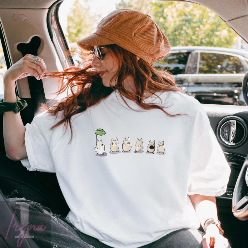 Op de afbeelding: Wit sweatshirt met ronde hals en een cartoonontwerp. Het ontwerp toont een wit personage met een groene bladeren paraplu, gevolgd door verschillende bruinachtige personages met verschillende uitdrukkingen. De trui is een casual stijl.