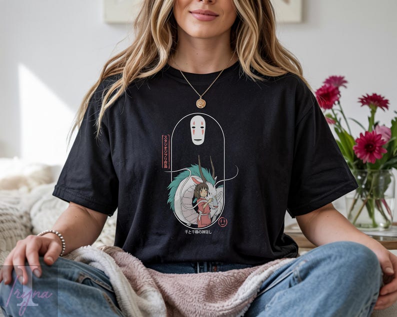 May include: Black t-shirt featuring a graphic from the animated film Spirited Away. The design includes the character No-Face, a dragon, and a girl in a red dress. Japanese text is also included in the design.