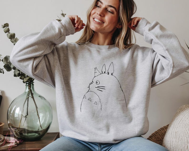 Op de afbeelding: Een lichtgrijs sweatshirt met een zwarte lijntekening van Totoro uit de animatiefilm My Neighbor Totoro. De illustratie toont Totoro en een kleiner Totoro-personage. De sweatshirt heeft lange mouwen en een ronde hals.