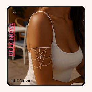 May include: Gold arm cuff with a delicate chain design. The armlet has a band above the elbow, with chains and rectangular charms hanging down. The brand name "Elif Nova" is displayed in the image.