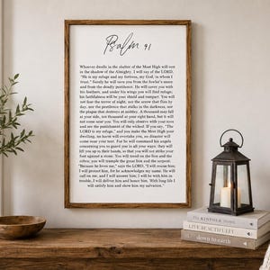 May include: A rectangular wall sign with a dark wood frame featuring the text of Psalm 91 in black lettering on a white background. The title Psalm 91 is written in a cursive script at the top, followed by the full biblical passage in a clear font.