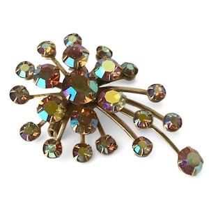 Può includere: Spilla vintage con un design floreale. La spilla presenta strass rotondi iridescenti nelle tonalità del marrone, giallo e verde acqua, montati su una base in metallo dorato. Gli strass sono disposti a forma di stella.