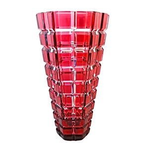 May include: A tall, ruby-red glass vase with a geometric, faceted design. The vase has a wide opening and tapers towards a dark base. The textured surface catches light, creating a sparkling effect. This decorative vase is suitable for floral arrangements.