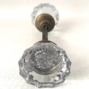May include: Clear glass door knob with a faceted design. The knob is attached to a brass stem and base. The door knob is a vintage style.