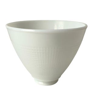 May include: A white ceramic bowl with a textured, grid-like pattern on the exterior. The bowl has a wide opening and tapers down to a small, rounded base. The bowl is likely used for serving food.