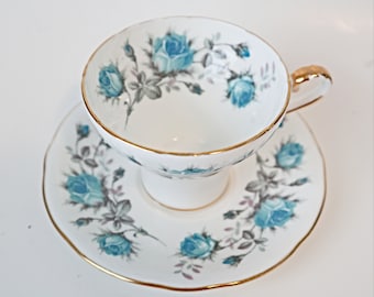 Può includere: Un set da tè bianco con un motivo floreale blu e grigio. La tazza e il piattino hanno un bordo dorato.