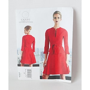 Pode incluir: Um padrão de costura para um vestido vermelho com detalhe de laço, com uma modelo vestindo o vestido. O padrão é rotulado "CHADO ralph rucci" e inclui o número do padrão V1317. O vestido tem decote em V e mangas três quartos.