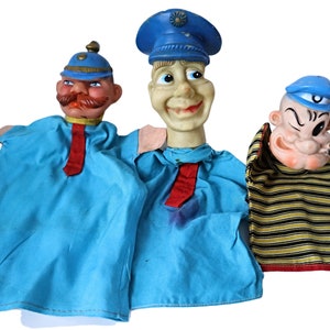 Puede incluir: Tres marionetas de mano vintage con detalles azules y rojos. Las marionetas están hechas de fieltro y plástico. La primera marioneta es un soldado con un sombrero azul y una corbata roja. La segunda marioneta es un policía con un sombrero azul y una corbata roja. La tercera marioneta es un marinero con un sombrero azul y una camisa a rayas.