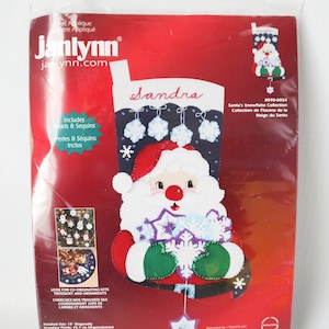 Peut inclure: Un kit de chaussette de Noël en appliqué de feutre représentant le Père Noël tenant des flocons de neige. La chaussette est rouge, verte, blanche et bleue avec un fond en feutre noir. La chaussette est personnalisée avec le nom "Sandra". Le kit comprend des perles et des paillettes.