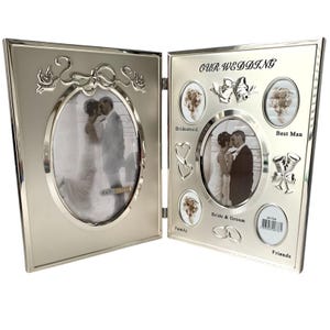 May include: Silver-colored, hinged photo frame with oval and circular openings. The frame is decorated with floral and ribbon designs. The text "OUR WEDDING" is at the top, with labels for "Bridesmaid", "Best Man", "Bride & Groom", "Family", and "Friends".