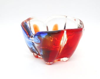 May include: A clear glass ashtray with a heart-shaped design. The ashtray features vibrant colors, including red, blue, and orange, creating a striking visual effect. The glass is shaped with curved edges and a textured surface.