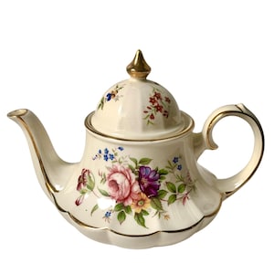May include: A cream-coloured ceramic teapot featuring a floral pattern with pink, purple, and yellow flowers, green leaves, and gold trim along the edges, handle, spout, and the pointed finial on the lid, which has a scalloped base design.