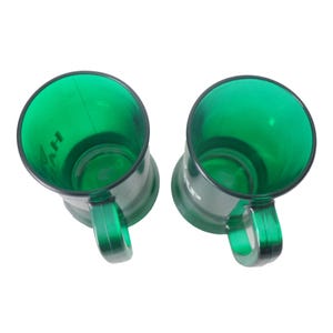 May include: Two green plastic mugs with black rims and handles are shown against a white backdrop. The mugs are transparent, revealing their interiors, and have a slightly tapered shape. The word "AH" is visible on the side of one mug.