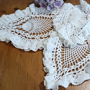 May include: Two white crocheted doilies with scalloped edges. The doilies are made with a delicate, intricate pattern.