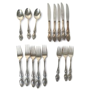 May include: An assortment of vintage silverware, comprising spoons, knives, and forks, presented on a white background. The cutlery features decorative handles and a polished finish, indicative of a formal dining set.