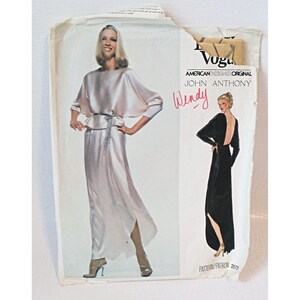 May include: Vintage sewing pattern for a long, flowing evening gown with a low back. The pattern is by John Anthony for American Vogue and features a white gown with a sash and a black gown with a plunging neckline.