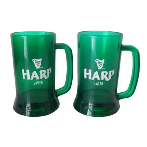 May include: Two green beer tankards with handles. Each tankard features the white text "HARP LAGER" and a harp logo. The tankards are made of a translucent green material.