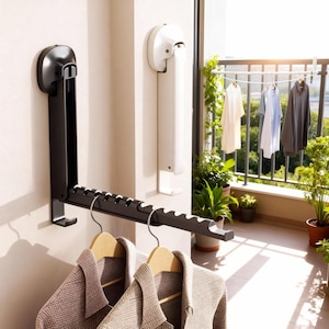 May include: A black wall-mounted clothes drying rack with a folding design. The rack has multiple slots for hangers and is shown with two jackets hanging on wooden hangers. A white wall-mounted unit is also visible.