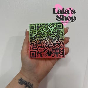 Peut inclure: Un code QR carré avec un dégradé de vert à rouge. Le code est tenu dans une main. Le logo Lala's Shop est en arrière-plan.