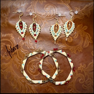 May include: Handmade jewelry set featuring two pairs of leaf-shaped earrings and two bracelets. The earrings and bracelets are adorned with red, turquoise, and gold beads. The jewelry is displayed on a brown, textured surface.