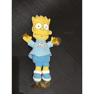 May include: A Bart Simpson plush doll with yellow skin, spiky hair, and large eyes. He wears a light blue shirt with "NO WAY MAN" text, blue shorts, and white-trimmed blue shoes. The doll holds two brass cymbals.