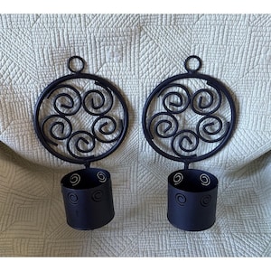 May include: A pair of matte black metal wall sconces, each featuring a circular frame with five internal spiral wire designs and a small hanging loop at the top. Below each circular frame is a cylindrical cup holder with spiral cutouts.