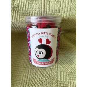 May include: A clear plastic jar with a lid, filled with a red plush toy. The jar has a label with a cartoon ladybug design and the text "Scentsy Bitty Buddy Love Bug" and "Rainbow Sherbet".